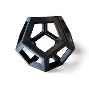 May include: A black geometric sculpture with a cube-like shape and multiple open sides. The sculpture is made of a solid material and has a smooth, matte finish.