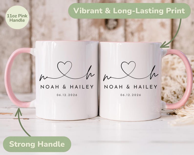 May include: Two white ceramic mugs with pink handles and interior rims. Each mug features a black heart design with the names "Noah & Hailey" and the date "06.12.2026". The mugs have a strong handle and a vibrant, long-lasting print.