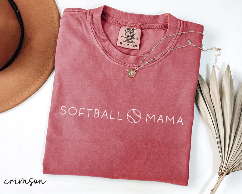 May include: Crimson red t-shirt with the text "SOFTBALL MAMA" and a white baseball graphic. The shirt is made of a soft, comfortable fabric.