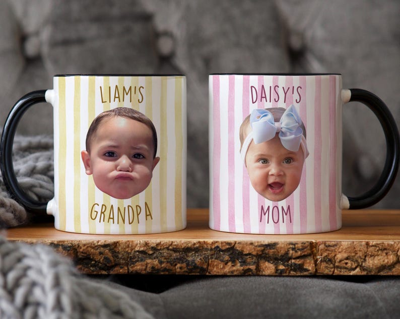 K&ouml;nnte beinhalten: Zwei Keramikbecher mit schwarzen Griffen und R&auml;ndern. Ein Becher hat ein gelb-wei&szlig; gestreiftes Muster mit einem Kindergesicht und dem Text "LIAM'S GRANDPA". Der andere Becher hat ein rosa-wei&szlig; gestreiftes Muster mit einem Kindergesicht und dem Text "DAISY'S MOM".