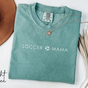 May include: Light green t-shirt with the text "Soccer Mama" and a soccer ball graphic.