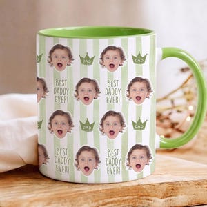 Może przedstawiać: Biały ceramiczny kubek z zielonym wnętrzem i uchwytem. Kubek ma powtarzający się wz&oacute;r twarzy dziecka, koron i tekstu "BEST DADDY EVER!" i "DAD" na paskowanym tle.