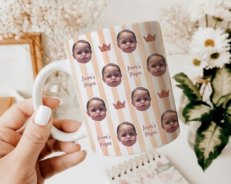 Może przedstawiać: Biały ceramiczny kubek z uchwytem, ​​z powtarzającym się wzorem twarzy dziecka, koron i napisem "Liam's Papa" na paskowanym tle. Kubek jest trzymany przez osobę.
