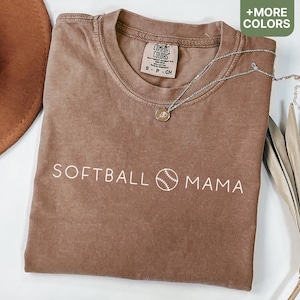 May include: A brown t-shirt with the text "SOFTBALL MAMA" and a baseball graphic in white. The shirt has a distressed look and is made of a soft, comfortable fabric.