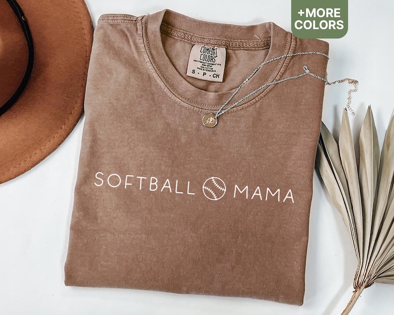 May include: A brown t-shirt with the text "SOFTBALL MAMA" and a baseball graphic in white. The shirt has a distressed look and is made of a soft, comfortable fabric.