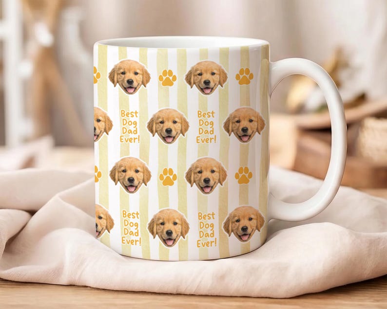 Może przedstawiać: Biały ceramiczny kubek z powtarzającym się wzorem pyszczk&oacute;w szczeniąt golden retriever, odcisk&oacute;w łap i napisem "Best Dog Dad Ever!" na ż&oacute;łto-białym tle w paski. Kubek ma biały uchwyt.