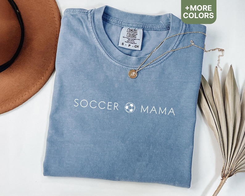 May include: A light blue t-shirt with the text "Soccer Mama" and a soccer ball graphic printed in white. The shirt is made of a soft, comfortable material.