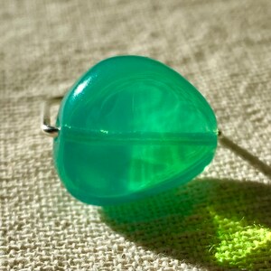 Può includere: Un rullo di giada verde con un manico d'argento. Il rullo è fatto di una pietra liscia e traslucida.