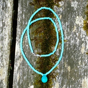 May include: A light blue beaded necklace with a teardrop-shaped turquoise pendant.