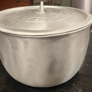 以下が含まれることがあります： 蓋付きの大きな銀色の調理鍋。鍋には2つのハンドルと蓋に小さなハンドルが付いています。鍋は金属製で、使い込まれたように見えます。鍋は調理用に設計されています。