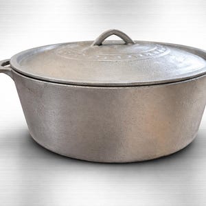 May include: A silver-coloured cast iron pot with a lid. The pot has a rounded shape with a handle on the lid and two handles on the sides. The lid has a decorative pattern around the edge.