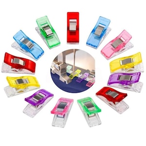 May include: Assortment of colourful plastic clips for sewing projects. The clips are transparent with a metal spring and come in red, blue, green, yellow, purple, and pink.