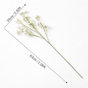 K&ouml;nnte beinhalten: Ein einzelner k&uuml;nstlicher Blumenstiel mit kleinen wei&szlig;en Bl&uuml;ten und gr&uuml;nen Stielen. Der Stiel ist 63 cm lang, der Bl&uuml;tenteil misst 25 cm. Die Blume ist vor einem wei&szlig;en Hintergrund platziert.