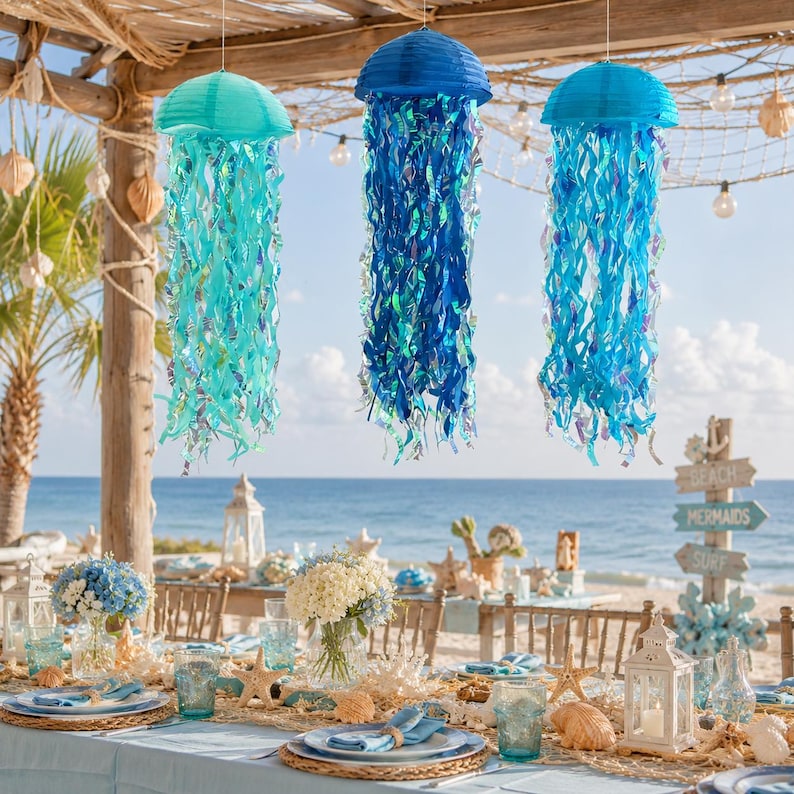 May include: Three hanging jellyfish decorations in shades of teal, dark blue, and bright blue. Each features a rounded paper lantern top with long, iridescent, shimmering ribbon tentacles that hang downward, creating a flowing aquatic effect.