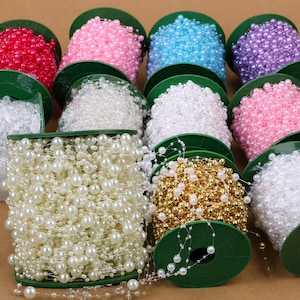 May include: Spools of decorative beaded garland in various colors, including red, pink, blue, purple, white, and gold. The beads are strung together and wound around green spools. Ideal for crafting and decorating.