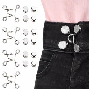 May include: A collection of silver metal hook and eye closures and magnetic button closures. The hook and eye closures are in a wavy design. The magnetic buttons are round and silver. The closures are shown on a pair of black denim jeans.