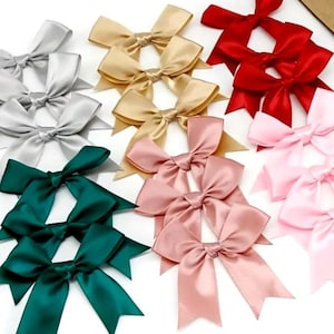 Op de afbeelding: Assortiment van satijnen strikken in verschillende kleuren, waaronder goud, zilver, rood, roze, groen en wit. De strikken zijn gebonden in een dubbele lus met puntige uiteinden.
