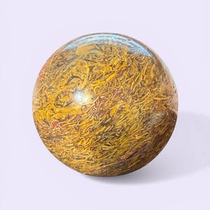 May include: A polished, spherical stone with a textured surface. The stone features a mix of yellow, brown, and reddish-brown hues, creating a unique, organic pattern. The sphere is smooth and reflective, suggesting a high level of craftsmanship.