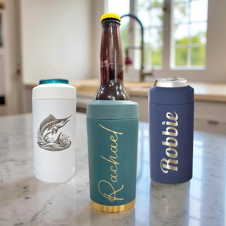 Puede incluir: Tres aislantes cil&iacute;ndricos para bebidas en blanco, verde azulado y azul marino. El aislante blanco presenta un gr&aacute;fico de un marl&iacute;n. El aislante verde azulado sostiene una botella de vidrio marr&oacute;n y est&aacute; personalizado con el nombre Rachael. El azul marino muestra el nombre Robbie.