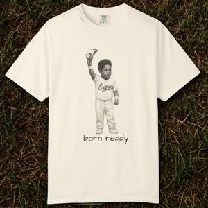 Peut inclure: T-shirt crème avec une illustration en noir et blanc d'un enfant en uniforme de baseball tenant une casquette. Le texte "born ready" est imprimé en dessous de l'illustration.