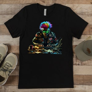 Peut inclure: T-shirt noir avec un graphisme coloré d'une personne aux cheveux arc-en-ciel et lunettes vertes, travaillant à un bureau. L'image comprend une paire de baskets beiges et une casquette de baseball grise.
