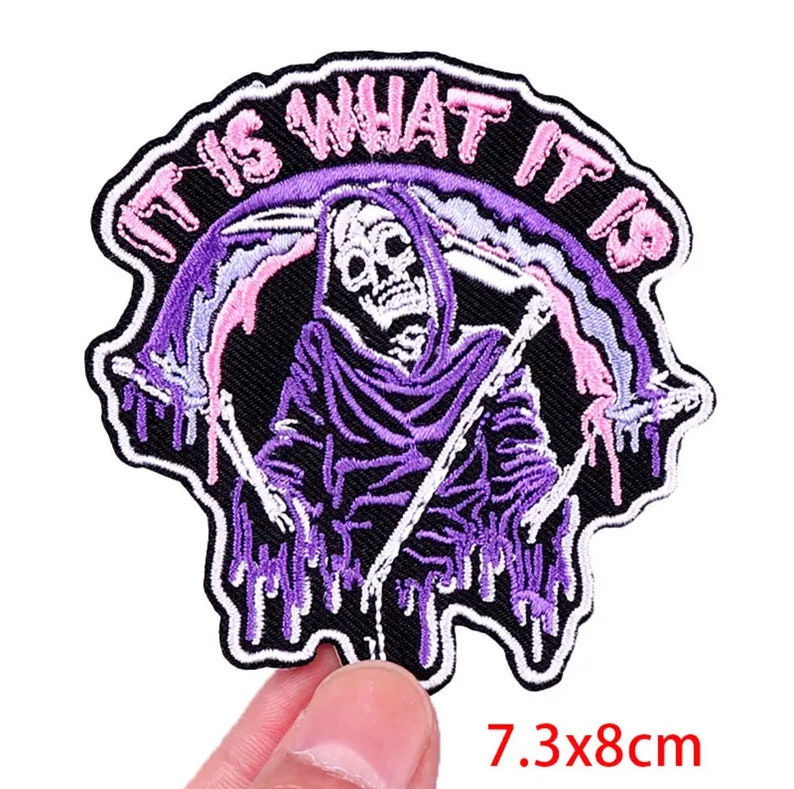 May include: Embroidered patch featuring a grim reaper in a purple hooded robe, holding a scythe. The patch has the text "IT IS WHAT IT IS" in pink. The patch measures 7.3 x 8 cm, or approximately 2.87 x 3.15 inches.
