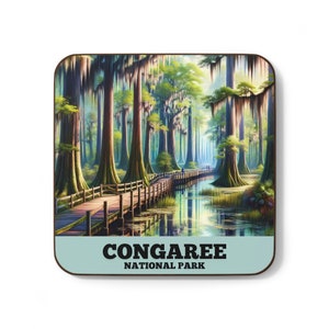 May include: A wooden coaster with a scenic image of a boardwalk through a swampy forest with tall trees and hanging moss. The text "CONGAREE NATIONAL PARK" is printed in black on a light blue background.