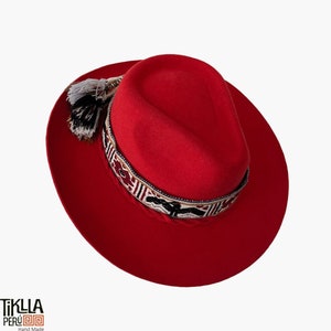 May include: A red felt fedora hat with a black and white patterned band and a black and white tassel. The hat is handmade in Peru.