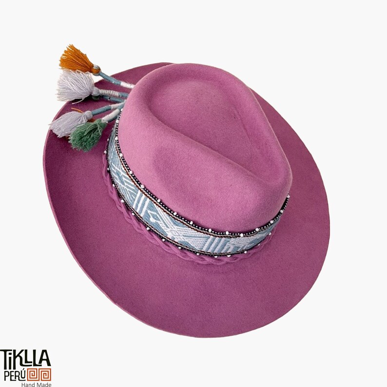 May include: A pink felt fedora hat with a blue and white patterned band and colourful tassels. The hat is handmade in Peru.