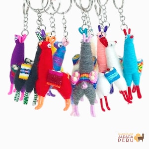 May include: A collection of colorful yarn-wrapped llama keychains, each featuring googly eyes and a small woven saddle. The llamas are rendered in various solid colors including red, blue, gray, white, and purple, all attached to silver metal key rings.
