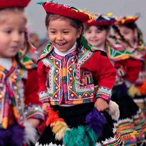 May include: Children in traditional Peruvian outfits, featuring red jackets with vibrant embroidery, black skirts, and red hats. The jackets display intricate patterns in multiple colours. The children are smiling and seem to be dancing, showcasing cultural attire.