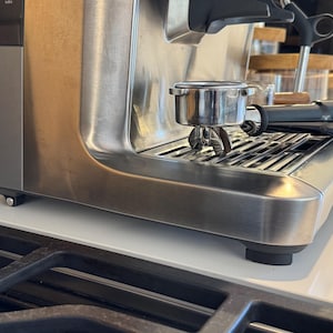May include: A stainless steel espresso machine with a portafilter and a drip tray. The machine is sitting on a white countertop.