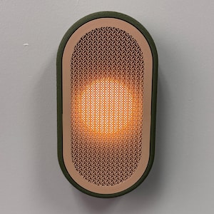 Peut inclure: Applique murale ovale avec un cadre vert et une fa&ccedil;ade en treillis de couleur cuivre. Le centre brille d'une lumi&egrave;re orange chaude. L'applique est fix&eacute;e sur un mur gris clair.