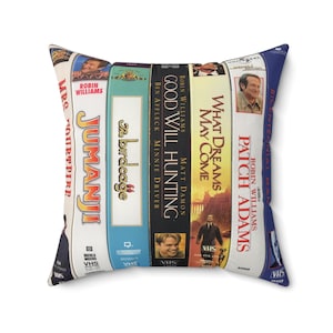 May include: Square pillow featuring a collage of VHS movie covers, including "Jumanji," "The Birdcage," and "Good Will Hunting." The pillow has a white background and a blue border, with the movie titles and actors' names visible.
