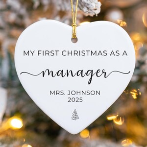 Peut inclure: Ornement de Noël blanc en forme de cœur avec une ficelle dorée. Le texte se lit « MY FIRST CHRISTMAS AS A manager MRS. JOHNSON 2025 » en écriture noire. Un petit graphique de sapin de Noël est en bas. Décorations de vacances festives.