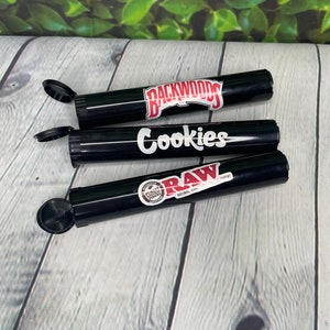 Op de afbeelding: Drie zwarte rolpapierbuizen met deksels. De buizen zijn gelabeld met "Backwoods", "Cookies" en "RAW Natural Unbleached Rolling Papers".