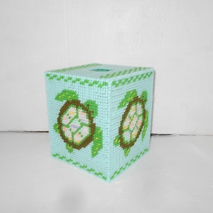 May include: A light blue tissue box cover with a green and brown turtle design. The turtle has a white shell with yellow and pink accents.