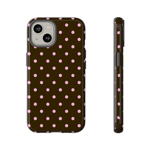 Pode incluir: Uma capa de telefone castanha com um padrão repetido de bolinhas cor-de-rosa. A capa é mostrada de frente e de lado, destacando o seu design e forma. A capa tem um recorte para a câmara e detalhes dos botões.