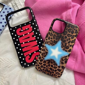 May include: Two smartphone cases. One case is black with white polka dots and the word SWAG in large red letters. The other case features a brown and black leopard print pattern with a central light blue star graphic with a white center.