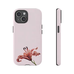 Pode incluir: Uma capa de telefone rosa com um design de uma única flor de lírio laranja. A capa tem um recorte de câmera preto e um botão preto na lateral.