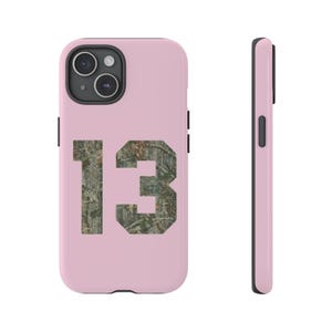Pode incluir: Capa de telefone rosa com um número 13 camuflado impresso nela.