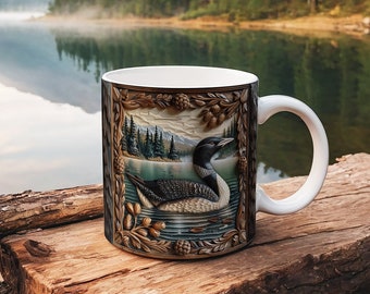 May include: White ceramic mug featuring a detailed illustration of a loon swimming on a lake, framed by a decorative border with pinecones and foliage. The background shows a serene lake scene with mountains and trees.