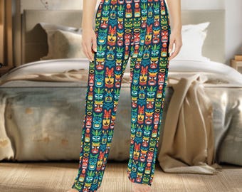 Könnte beinhalten: Marineblaue Schlafanzughose mit einem sich wiederholenden Muster aus bunten Tiki-Masken. Die Masken haben rote, gelbe, grüne und blaue Akzente. Die Hose ist aus einem weichen, bequemen Material.