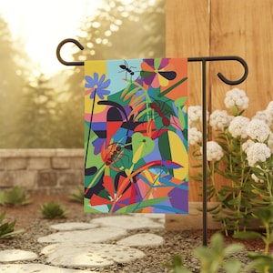 Könnte beinhalten: Eine farbenfrohe Gartenflagge mit geometrischem Design, das Ameisen, Blumen und Blätter zeigt. Die Flagge ist an einem schwarzen Metallständer befestigt.