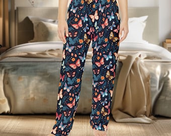 Puede incluir: Pantalones de pijama azul oscuro con un colorido estampado de mariposas y flores. Las mariposas son en tonos rosa, naranja y azul, sobre un fondo de hojas verdes y flores naranjas. Los pantalones tienen un corte holgado.
