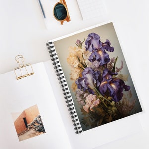 May include: A spiral bound notebook with a colorful illustration of purple and white irises on the cover. The background is a light beige color.