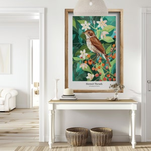 May include: A framed art print featuring a Hermit Thrush bird illustration. The artwork showcases a brown bird perched on a branch with red berries and white flowers, set against a backdrop of green foliage. The print is displayed on a white table with decorative baskets.