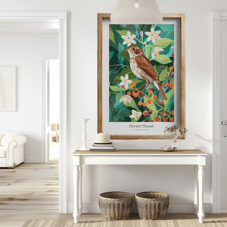 May include: A framed art print featuring a Hermit Thrush bird illustration. The artwork showcases a brown bird perched on a branch with red berries and white flowers, set against a backdrop of green foliage. The print is displayed on a white table with decorative baskets.