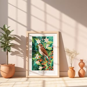 May include: A framed art print featuring a Hermit Thrush bird illustration. The artwork showcases a brown bird perched on a branch with berries and white flowers, set against a green background. The print is in a light wood frame, displayed near potted plants.
