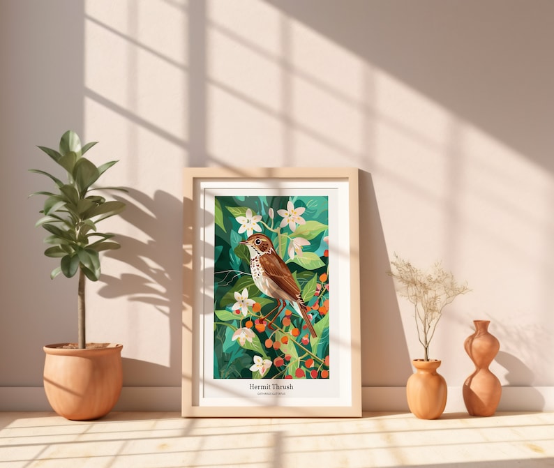 May include: A framed art print featuring a Hermit Thrush bird illustration. The artwork showcases a brown bird perched on a branch with berries and white flowers, set against a green background. The print is in a light wood frame, displayed near potted plants.